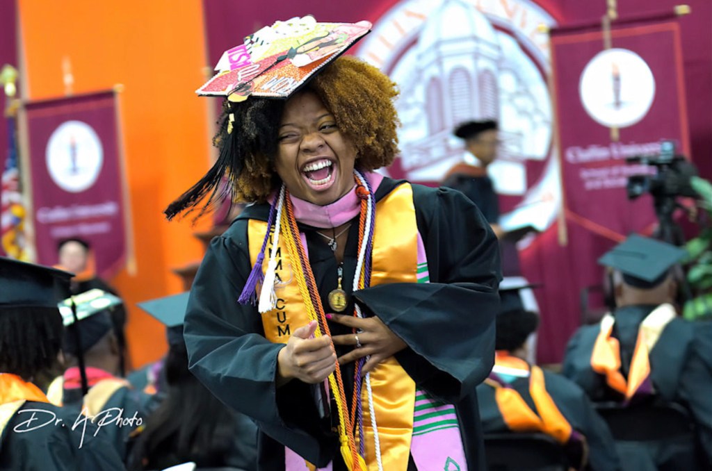 Student smiling proudly in graduation cap and gown, celebrating achievement.