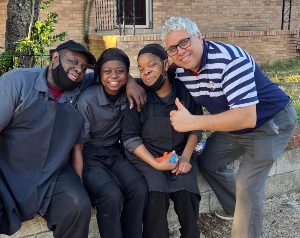 Luis Almeida standing with cafeteria workers, smiling together in a group photo.